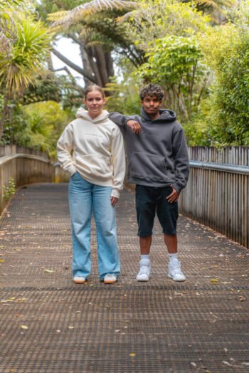 Two friends on a bush boardwalk wearing Pray Hoodies in Peach and Grey